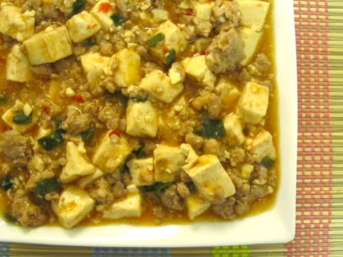 Mapo tofu served on a white plate, featuring soft tofu cubes, ground meat, chopped green onions, and a spicy sauce.