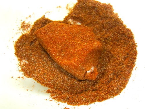 Chunk of pork coated in a dry spice rub with chili powder and seasonings, prepared for orange beer braised pork carnitas.