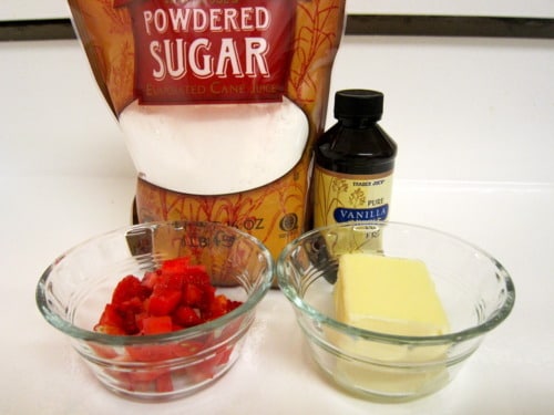Ingredients for strawberry filling, including powdered sugar, vanilla extract, chopped strawberries, and butter, arranged on a counter.
