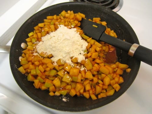 Diced apples being cooked with flour and spices in a skillet, prepared for apple fritter muffins.