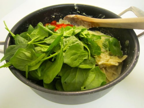 Fresh spinach and chopped tomatoes added to a pot of creamy lemon pasta, ready to be mixed and cooked together.