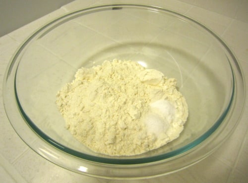 Glass mixing bowl with flour, baking powder, and salt for lemon poppy seed pound cake muffins.