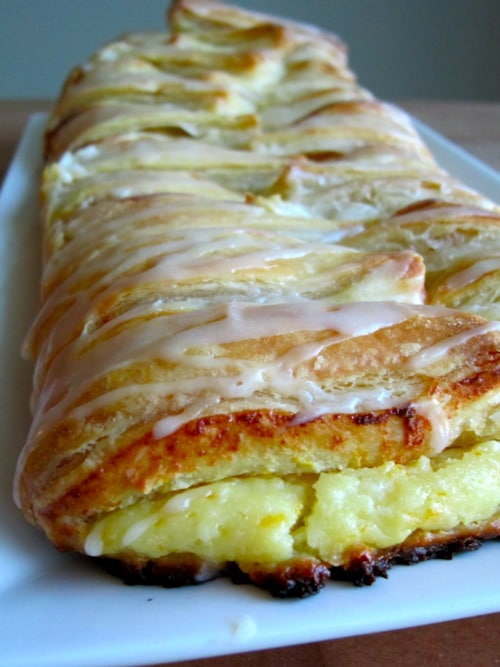 Homemade orange cheese danish with a golden, flaky crust and icing drizzle, served on a white plate.