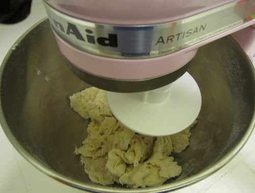 Pizza dough being mixed in a stand mixer with a dough hook attachment for cast iron skillet deep dish sausage pizza.