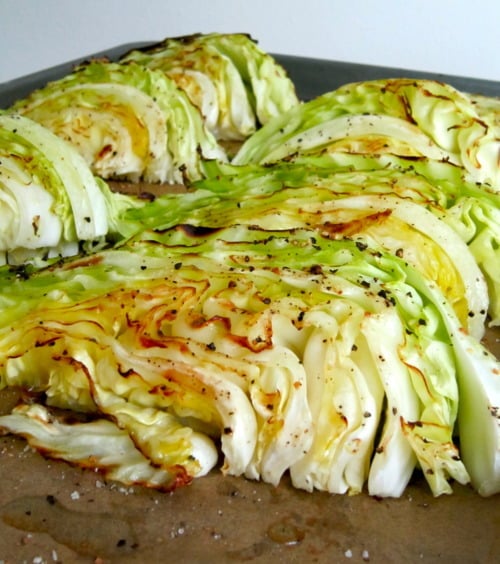 Roasted cabbage wedges seasoned with salt and pepper on a baking sheet.