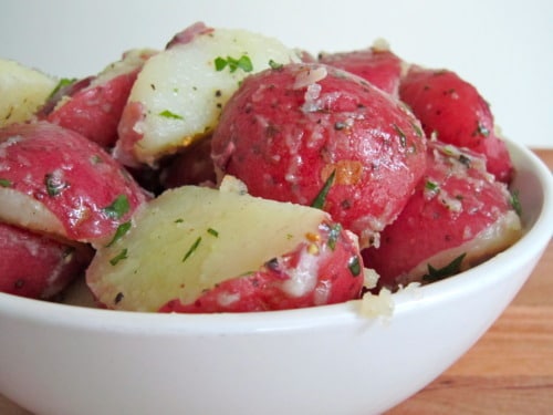 Bowl of cooked red potatoes seasoned with herbs and onions, served as a side dish for baked honey mustard corned beef with roasted cabbage.