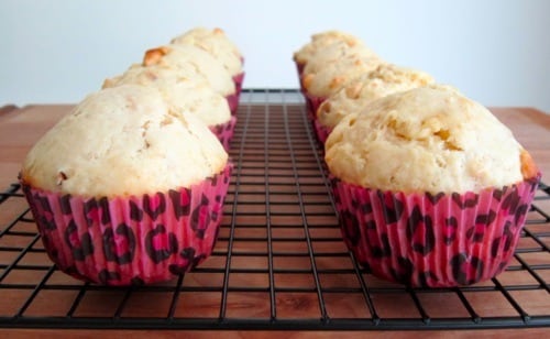 White chocolate chip macadamia nut muffins in pink leopard-print liners cooling on a black wire rack.