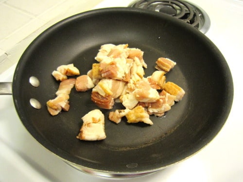 Chopped raw bacon in a black skillet on a stovetop, ready to be cooked for loaded potato skins.