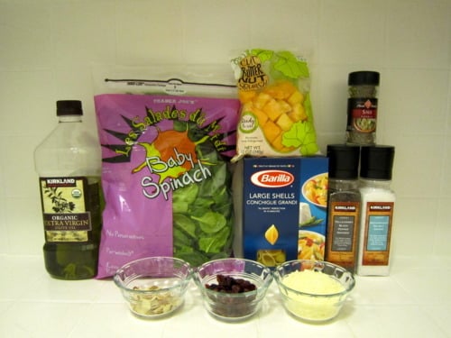 Ingredients for butternut squash pasta including baby spinach, pasta shells, olive oil, dried cranberries, almonds, Parmesan cheese, and seasonings.