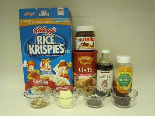 Assorted ingredients for a no-bake snack, including Rice Krispies cereal, oats, Nutella, vanilla extract, honey, and small bowls of butter, chocolate chips, and raisins.