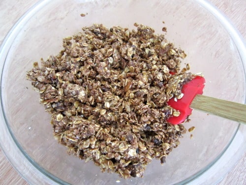 Granola mixture with oats, Nutella, and mix-ins stirred in a glass bowl with a red spatula for crunchy Nutella granola bars.