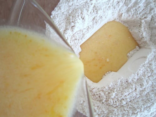 Wet ingredients being poured into a well of dry ingredients for hot cross bun muffins.