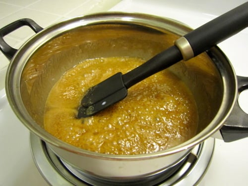 Caramel mixture bubbling in a saucepan, being stirred with a spatula for Samoas cupcakes.
