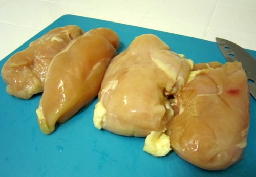 Raw chicken breasts stuffed with a filling, placed on a cutting board for preparation.