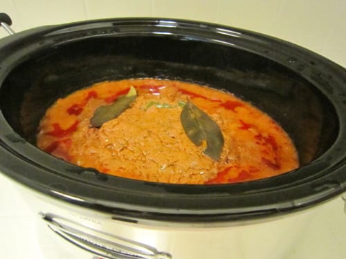 Chicken tikka masala cooking in a slow cooker with a rich orange sauce and bay leaves on top.