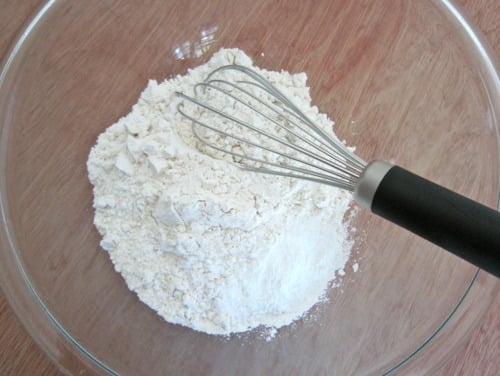 Glass bowl with flour and a whisk, prepared for sugar-crusted strawberry blueberry muffins.