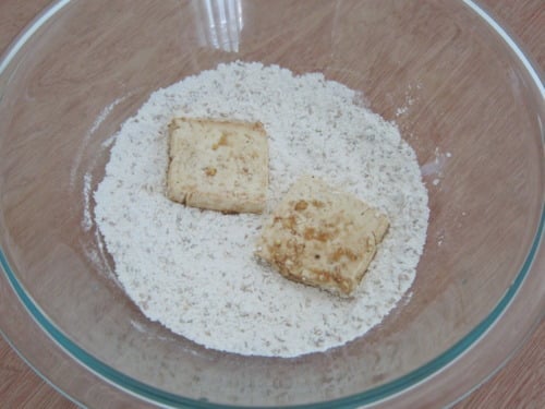 Tofu pieces coated in flour mixture in a glass bowl for sesame crusted tofu.