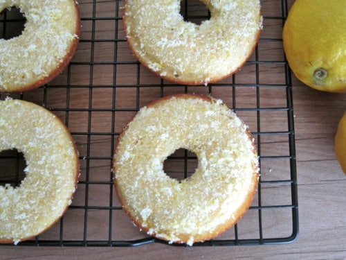 Honey cornbread donuts topped with lemon zest cooling on a wire rack, with fresh lemons on the side.