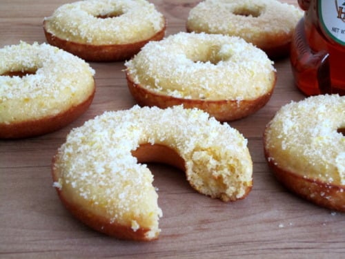 Honey cornbread donuts topped with lemon zest and sugar, with one donut showing a bite taken out.