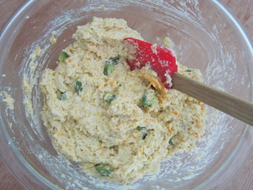 Jalapeño cheddar Parmesan cornbread batter mixed in a glass bowl with visible chopped jalapeños and shredded cheese.