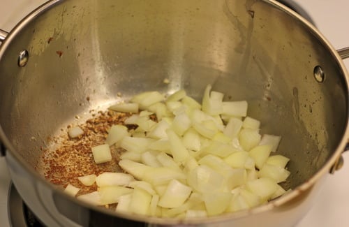 Chopped onions sautéing in a stainless steel pot for pancetta fried rice.