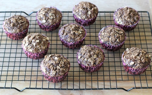 Mocha oatmeal muffins with oat crumble topping, cooling on a wire rack in pink paper liners.