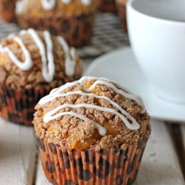 A baked pumpkin streusel muffin topped with drizzled vanilla glaze.