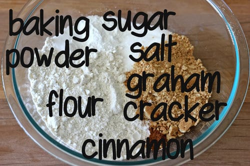 Dry ingredients for strawberry cheesecake graham cracker muffins in a glass bowl, including flour, baking powder, sugar, salt, graham cracker crumbs, and cinnamon, labeled with text.