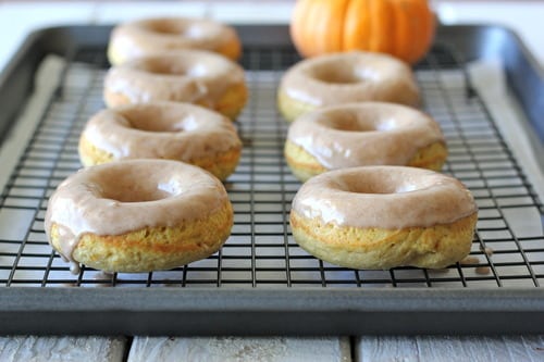 Baked pumpkin donuts with maple glaze cooling on a wire rack with a small pumpkin in the background.