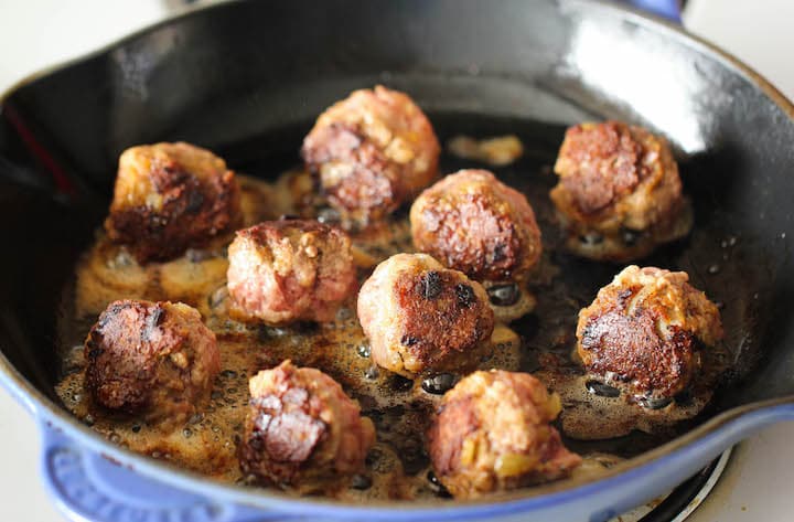 Rolled Swedish meatballs browning in a hot skillet.