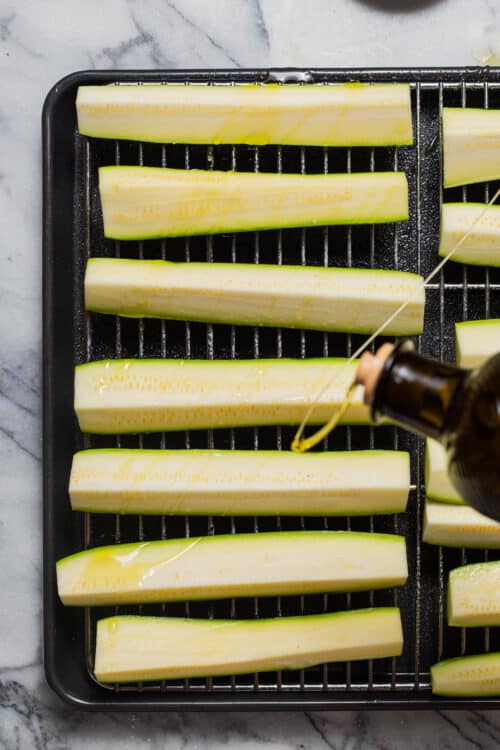 Drizzling olive oil over zucchini before baking