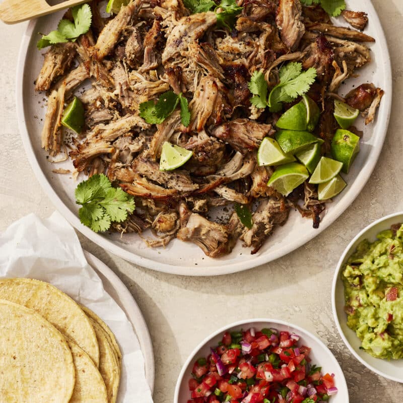 Slow cooker pork carnitas served with tortillas, guacamole, and salsa