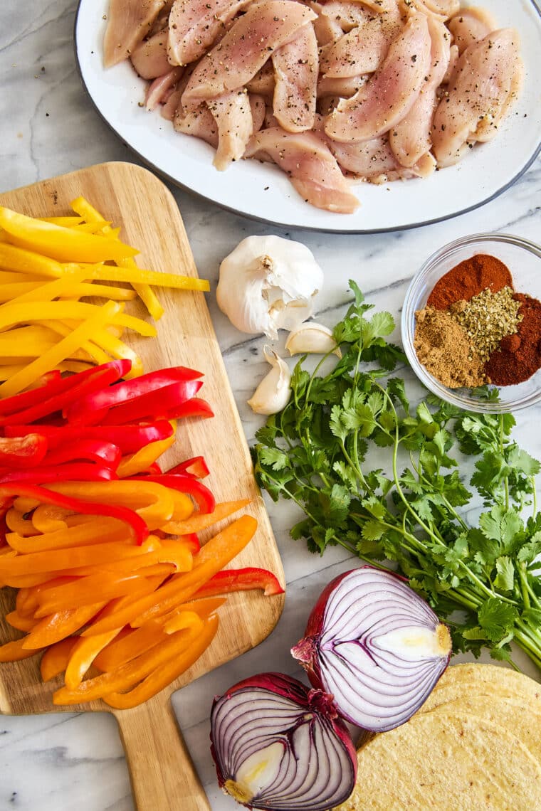 Plated chicken fajitas with roasted bell peppers, red onions, sliced chicken, cilantro, and a lime wedge on a white dish.