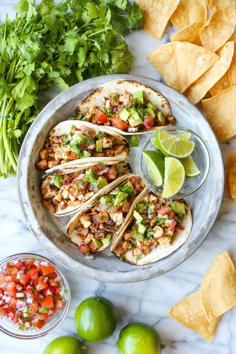 Easy chicken tacos recipe served with pico de gallo, avocado, cilantro, and lime wedges