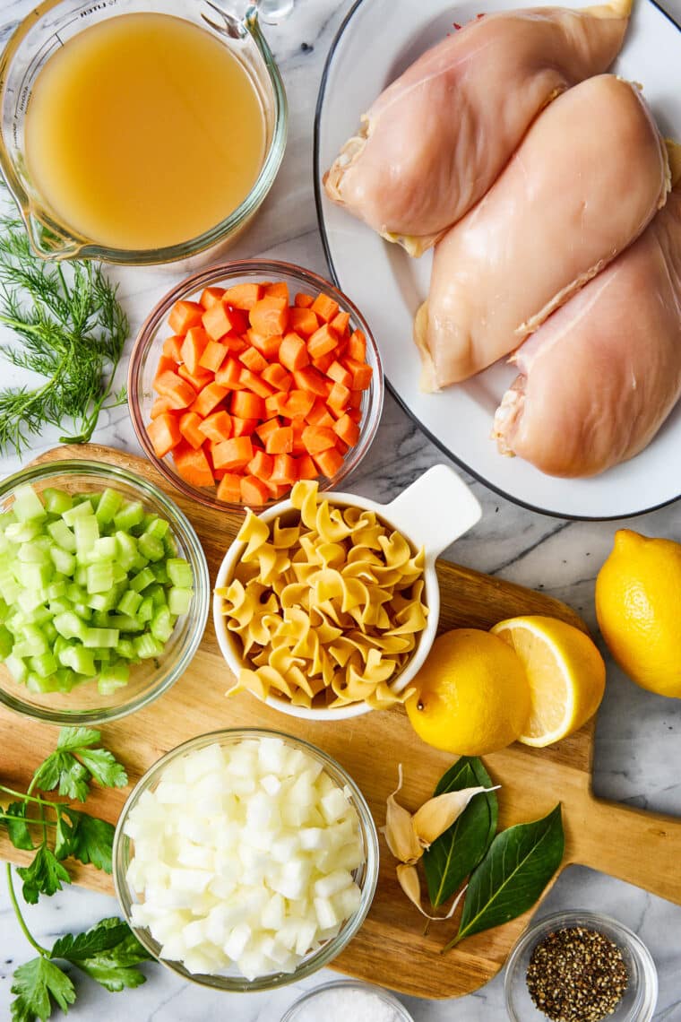 "A bowl of chicken noodle soup on a white surface, featuring shredded chicken, egg noodles, carrots, and celery in a savory broth, with a spoon nearby.